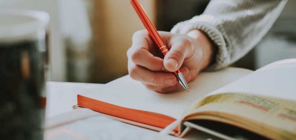 person holding on red pen while writing on book
