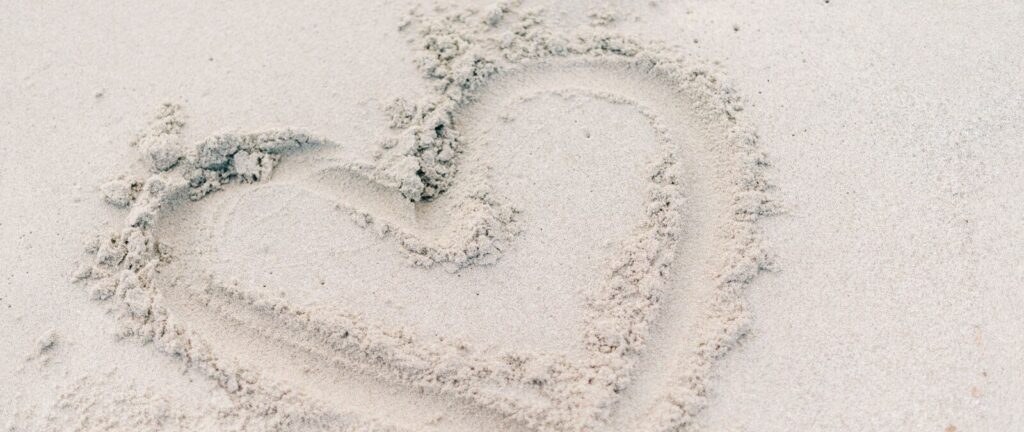 person forming heart on sand using right foot