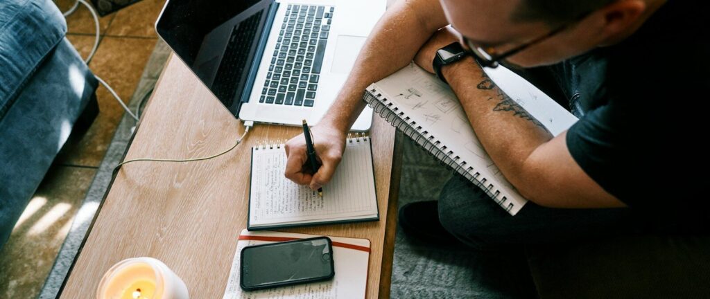 man in black t-shirt writing on white paper