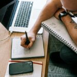 man in black t-shirt writing on white paper