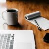 MacBook Pro, white ceramic mug,and black smartphone on table