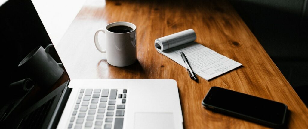 MacBook Pro, white ceramic mug,and black smartphone on table