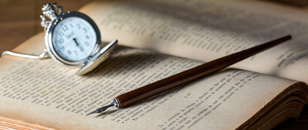 brown pen on top of book beside gray pocket watch