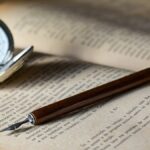 brown pen on top of book beside gray pocket watch