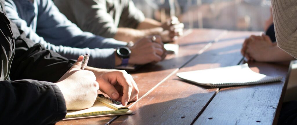 people sitting on chair in front of table while holding pens during daytime