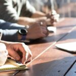 people sitting on chair in front of table while holding pens during daytime