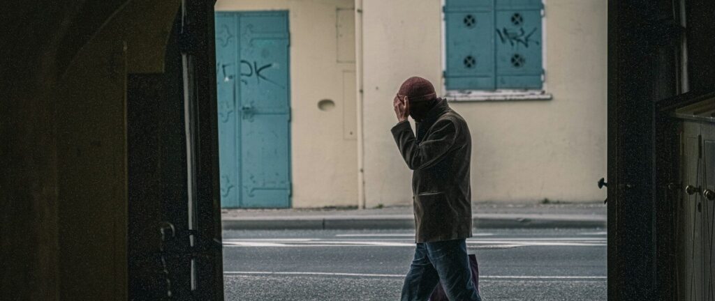 man in black jacket and blue denim jeans standing on sidewalk during daytime