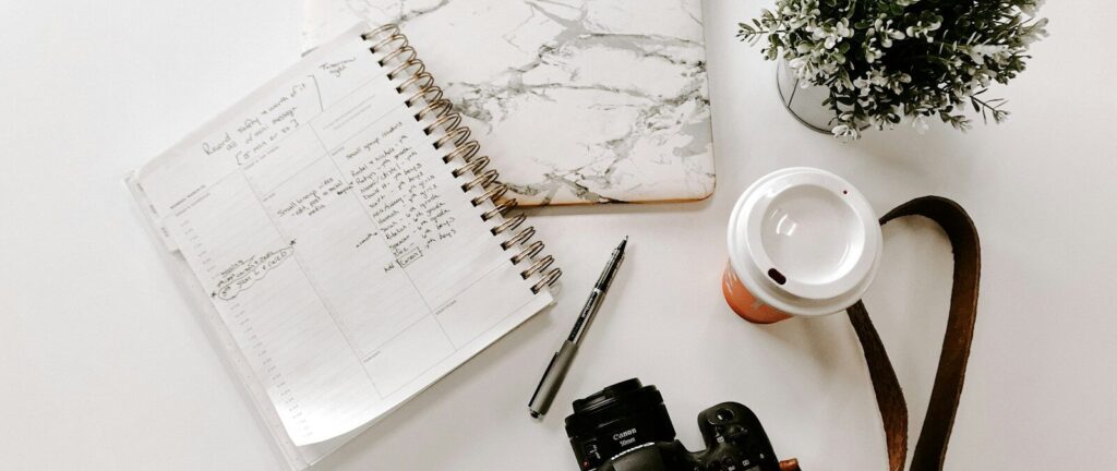 black nikon dslr camera on white notebook beside white ceramic mug