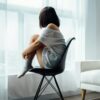 woman sitting on black chair in front of glass-panel window with white curtains