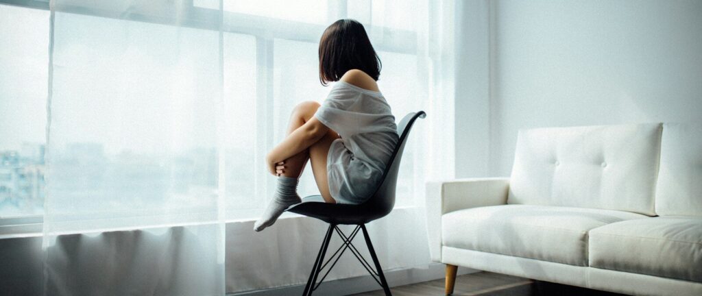 woman sitting on black chair in front of glass-panel window with white curtains