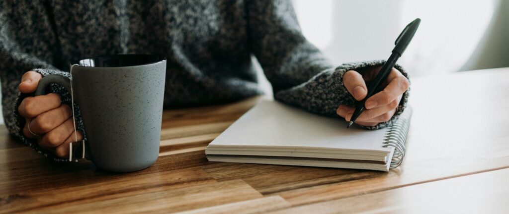 a person holding a pen and writing on a notebook