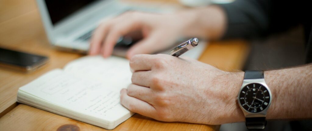 man sitting while writing on notebook