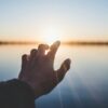 landscape photography of person's hand in front of sun