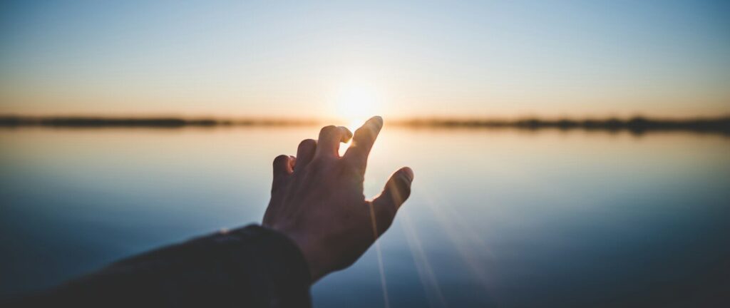 landscape photography of person's hand in front of sun