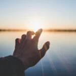 landscape photography of person's hand in front of sun